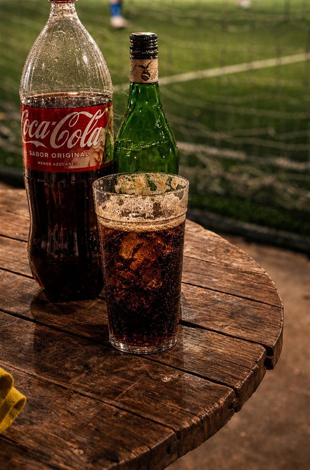 Una gaseosa fría en la mesa, con la cancha de fondo